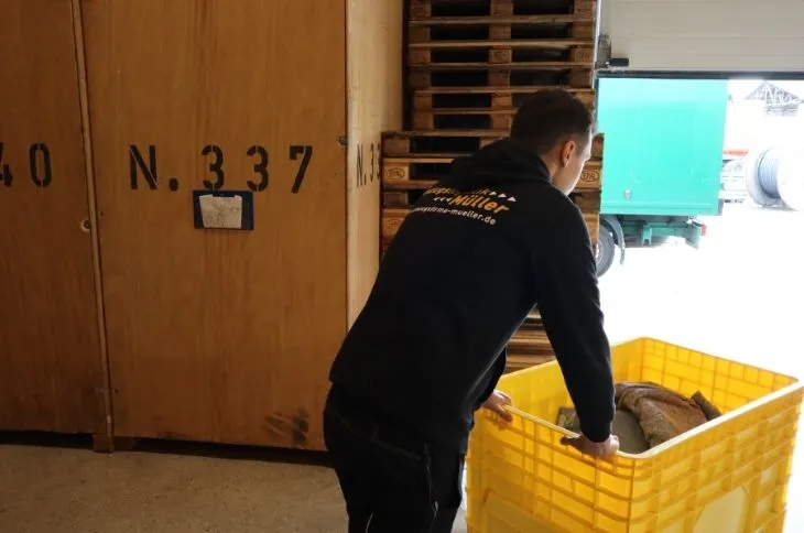 umzugshelfer schiebt gelbe transportbox im lager